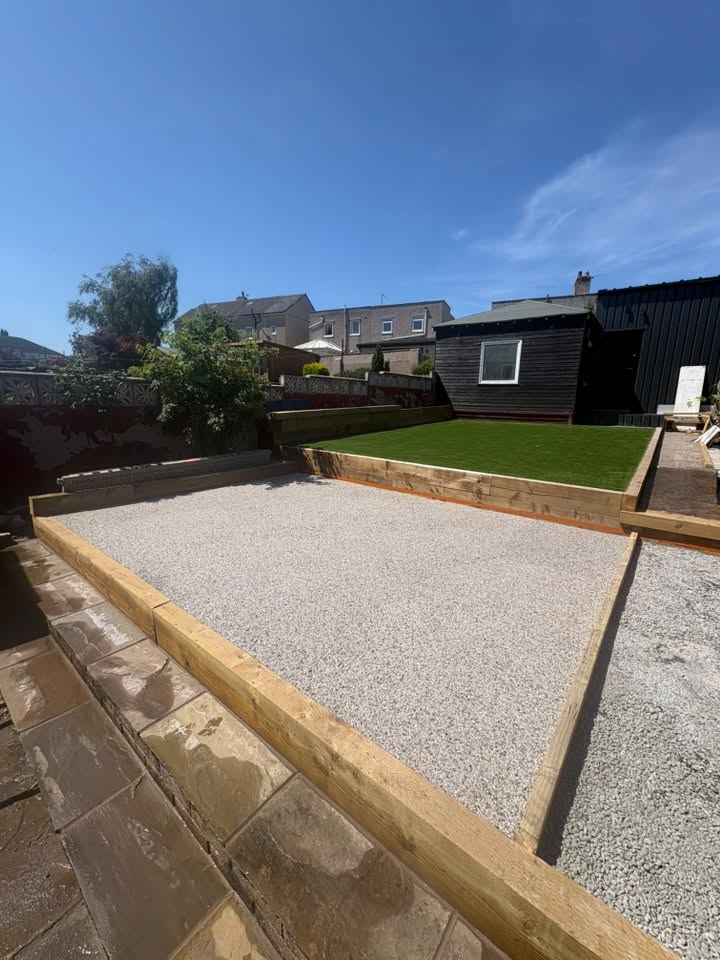 Tiered garden in Seaton with timber sleepers, gravel and artificial turf